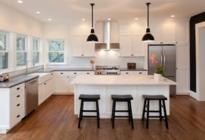 Bright and beautiful new, modern kitchen in luxury home with low hanging lights above a white kitchen island