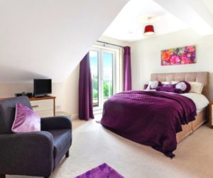purple bedroom with a leather seat and floral wall art