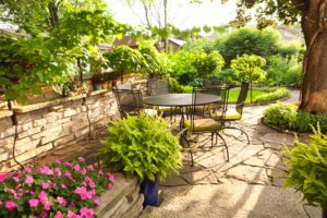 Landscpaed back graden with shrubs, trees and flowers, along with outdoor seating and table on a summer day