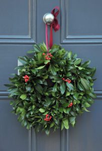 A decorative festive Christmas holly wreath tied to a door knocker in the winter